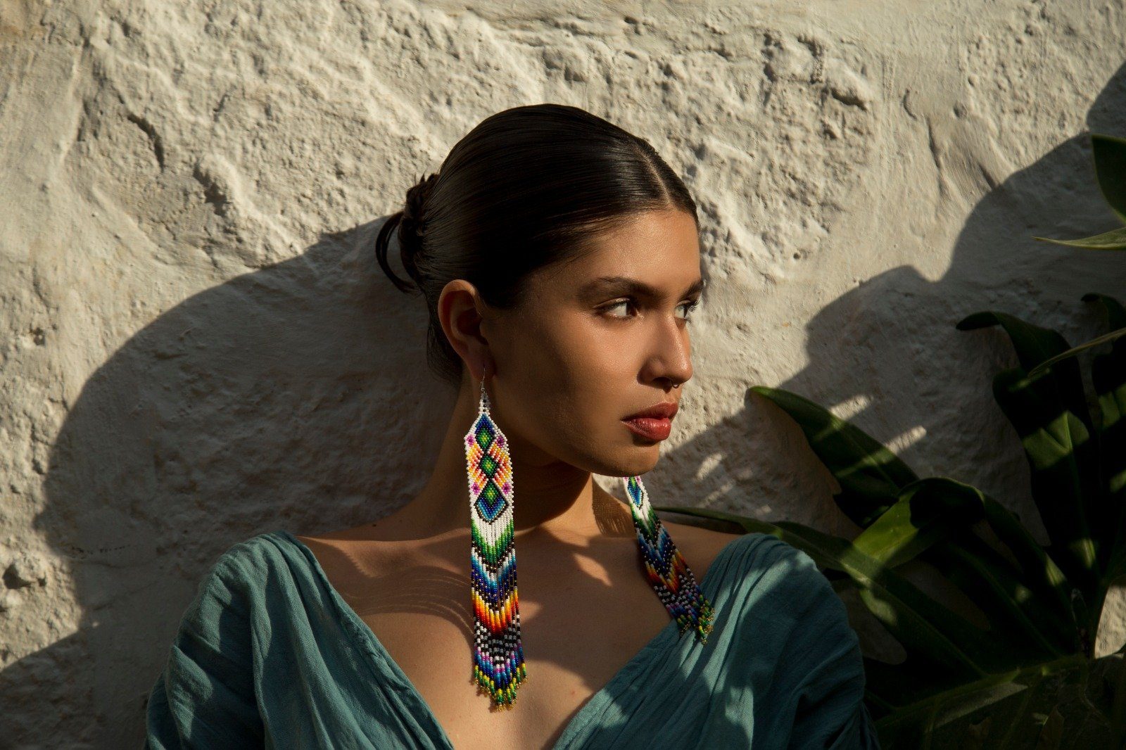 Woman wearing long rainbow beaded earrings with green dress in front of stone wall