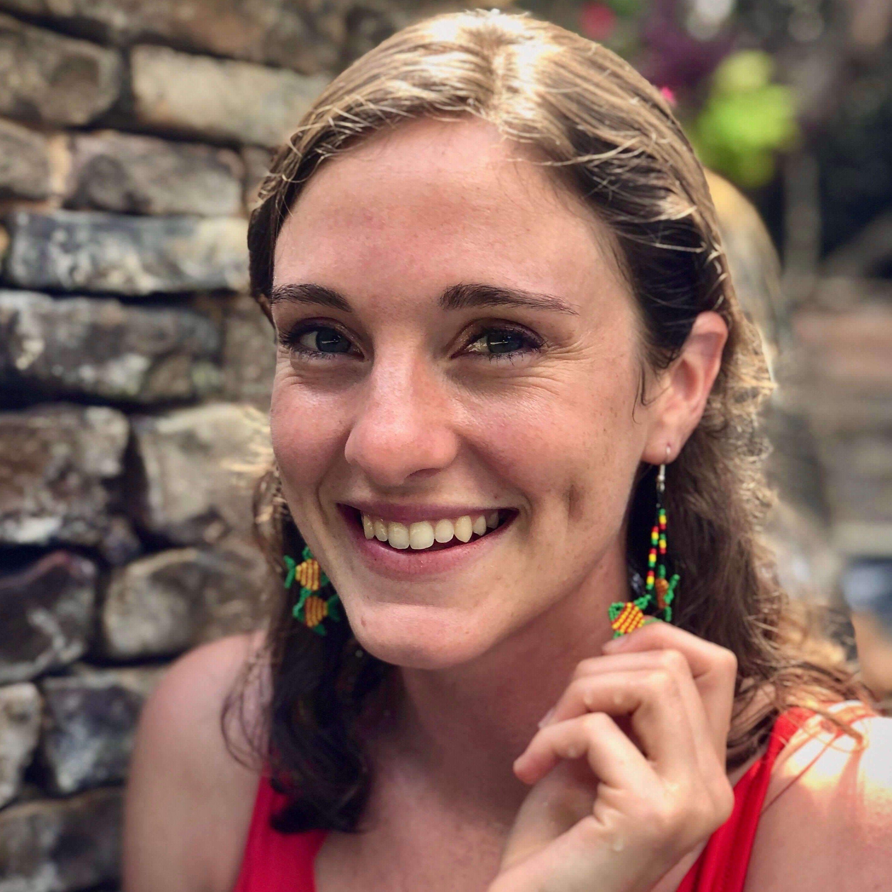 woman smiling wearing green yellow fish dangling beaded earrings