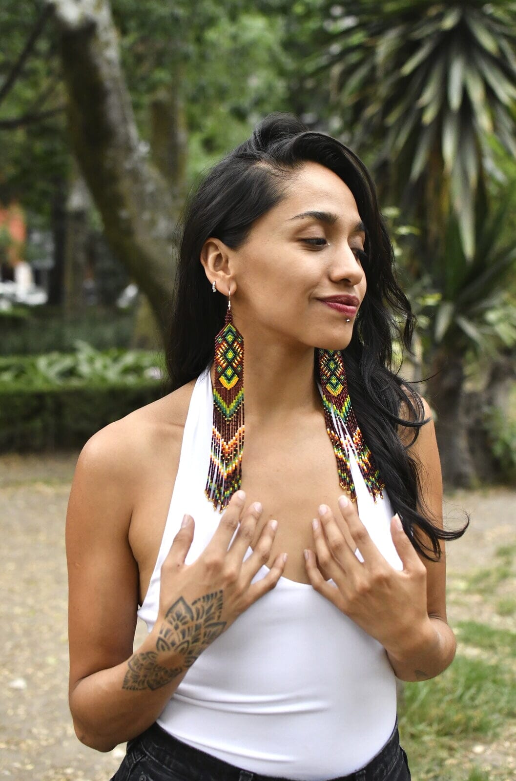 Woman wearing long brown and green beaded earrings outside with white shirt