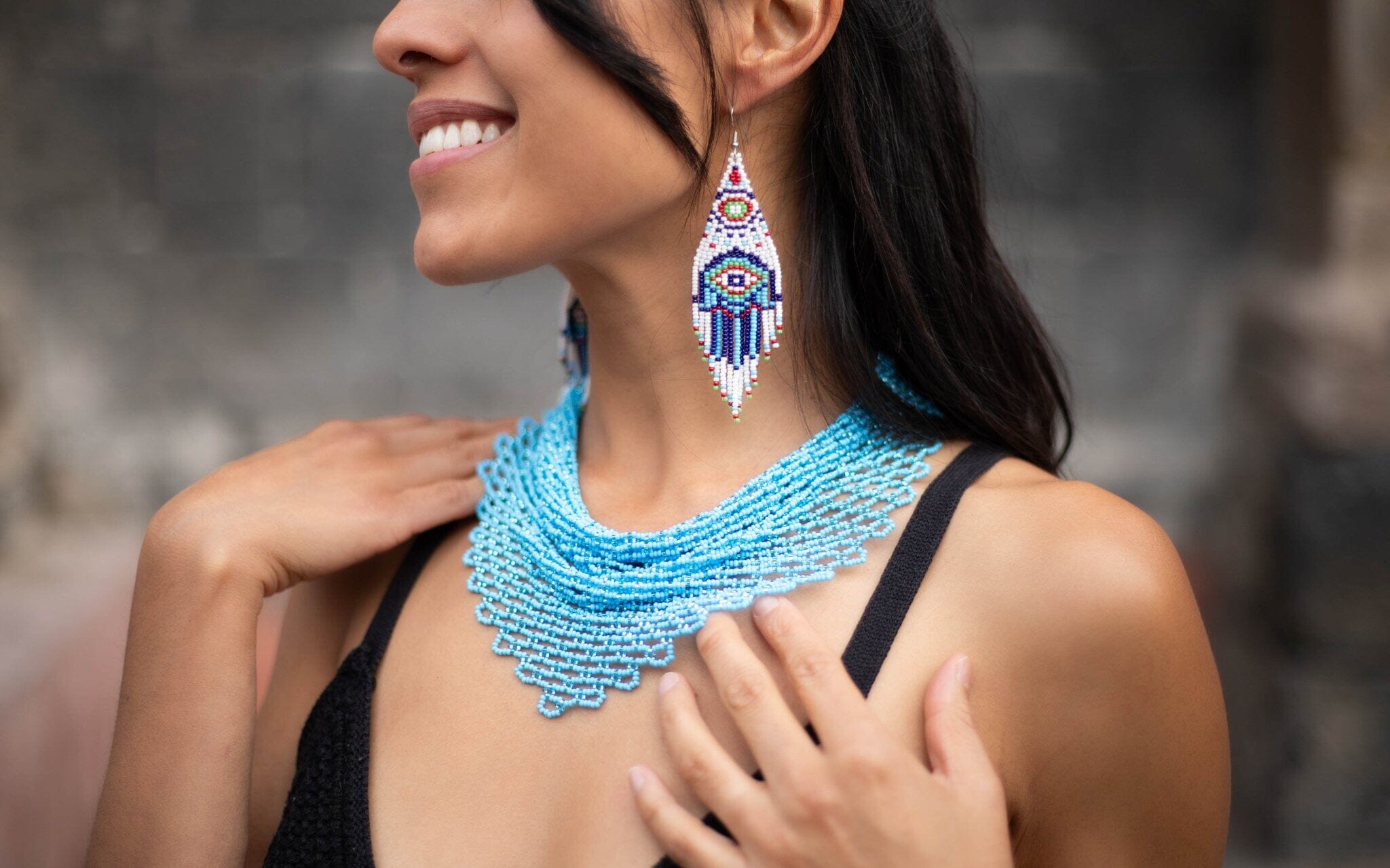 A woman wearing an Azore blue beaded scarf choker necklace, Native American jewelry, and blue Hamsa beaded earrings.