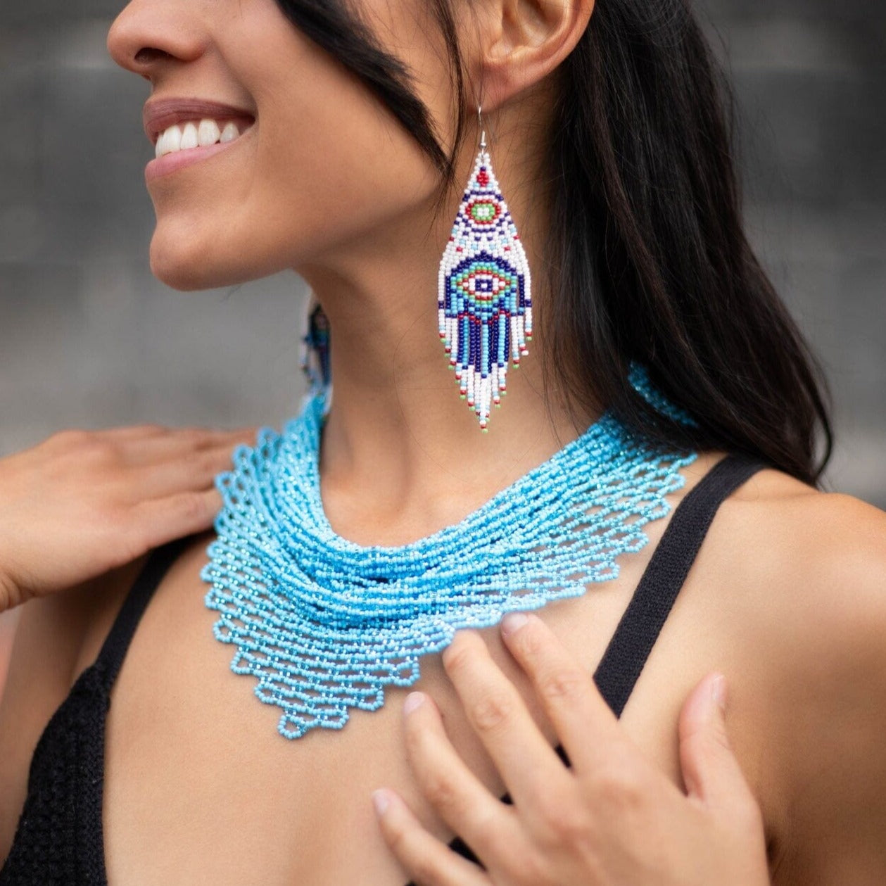 A woman wearing an Azore blue beaded scarf choker necklace, Native American jewelry, and blue Hamsa beaded earrings.