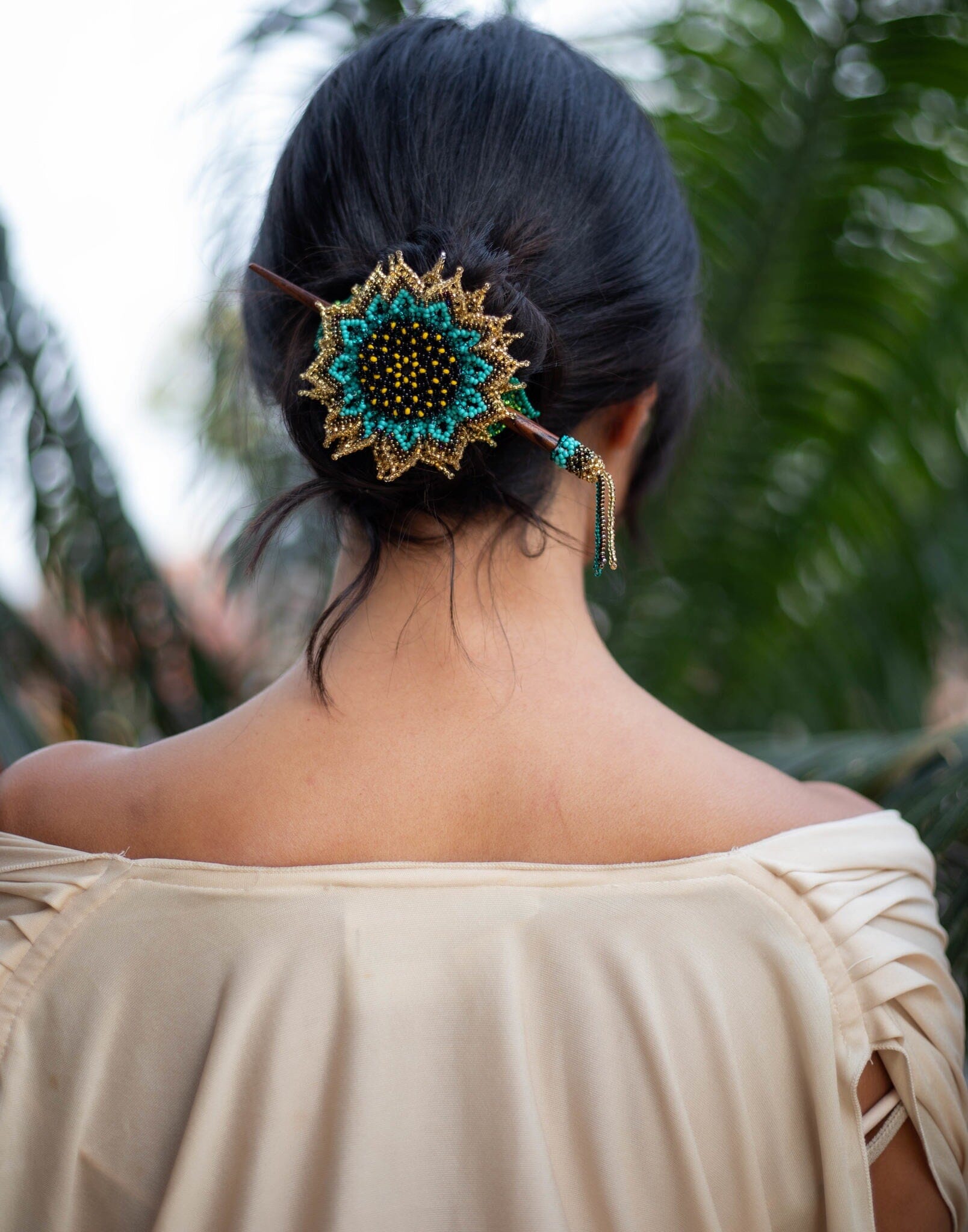 A woman wearing a statement piece of Native American jewelry: a blue sunflower gold, green, and yellow beaded hair barrette and pin.