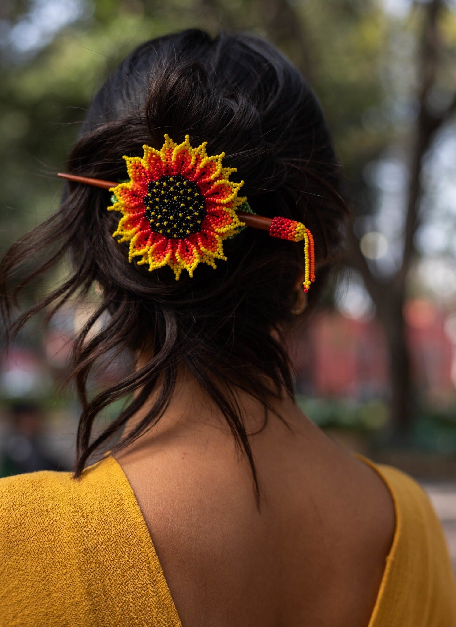 A bright sunflower petal yellow, red, green beaded hair barrette hairpiece, a Native American jewelry piece in dark hair.