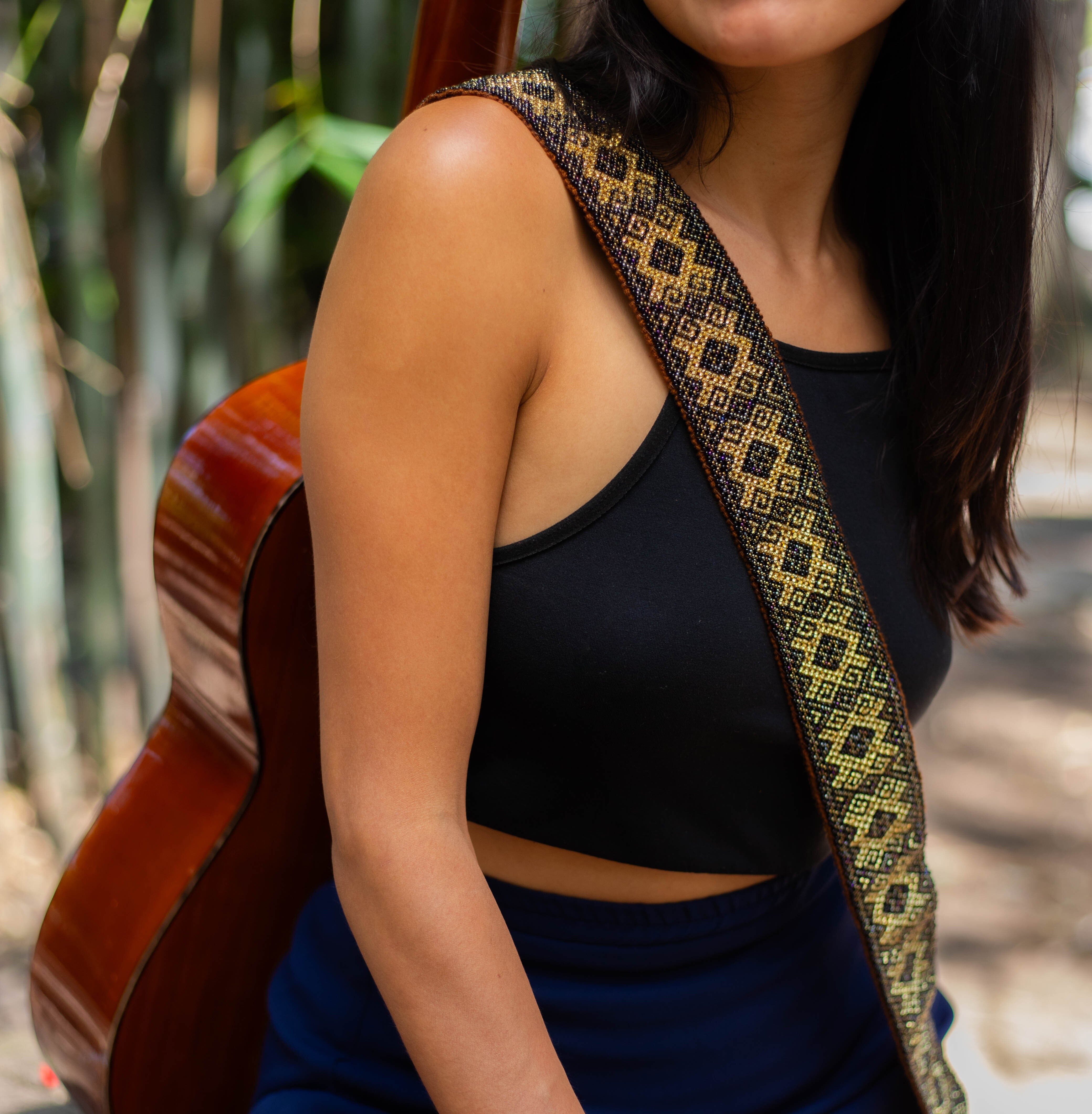 A woman wearing a Grecian Gold handmade beaded Guitar Strap, black and gold mosaic, adjustable leather on a guitar.