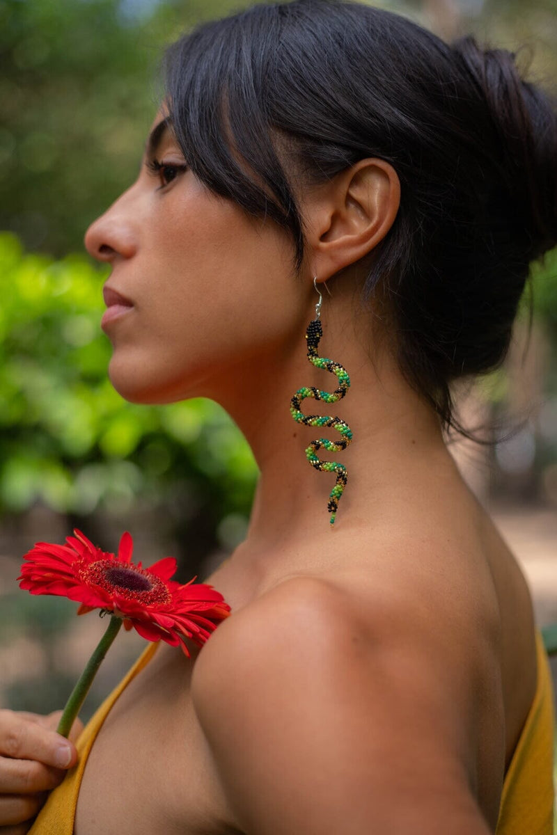 woman wearing green black gold slithering snake beaded earrings holding red flower
