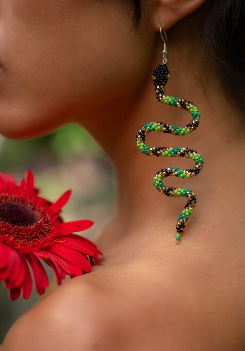 woman wearing green black gold snake beaded earrings holding red flower