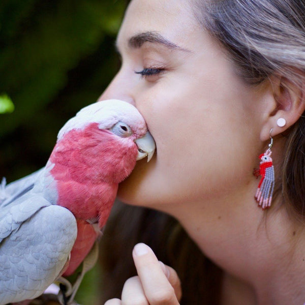 woman wearing pink red gray bogie galah bird earrings kissing bogie the galah