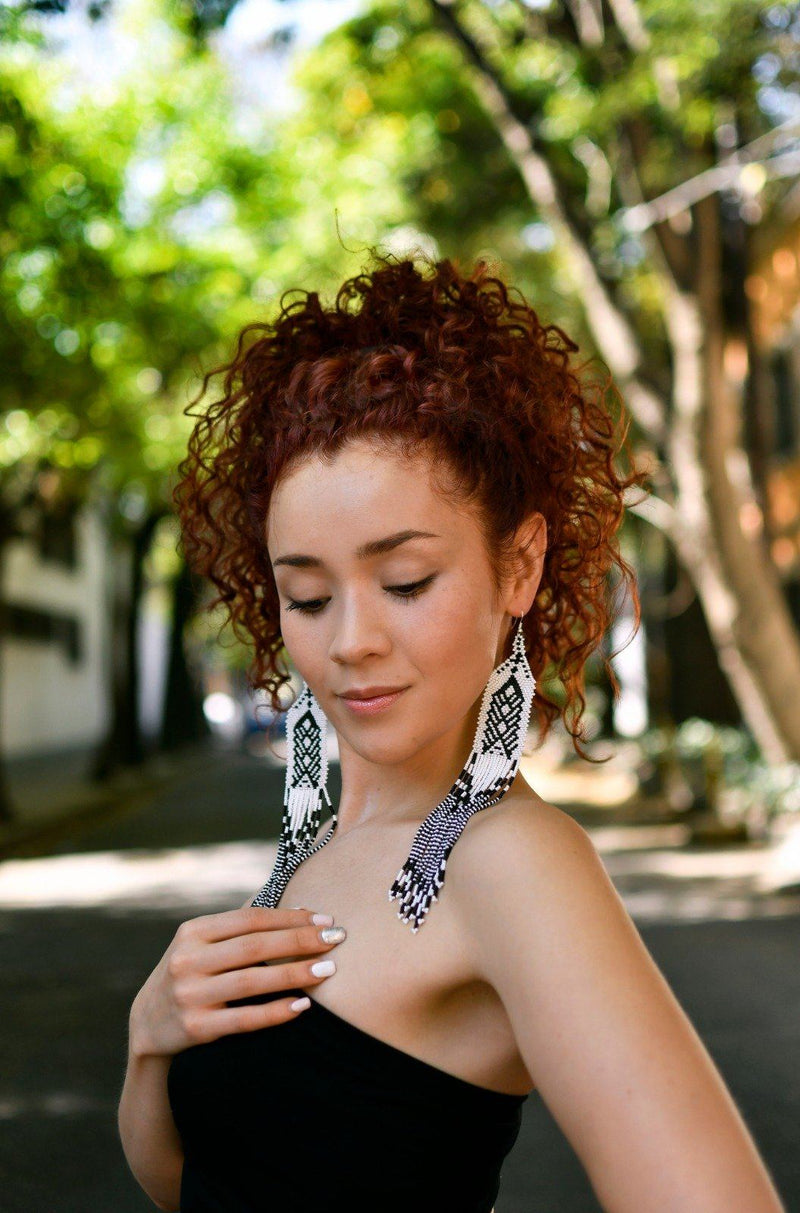 Woman wearing long white beaded earrings standing in sunny street