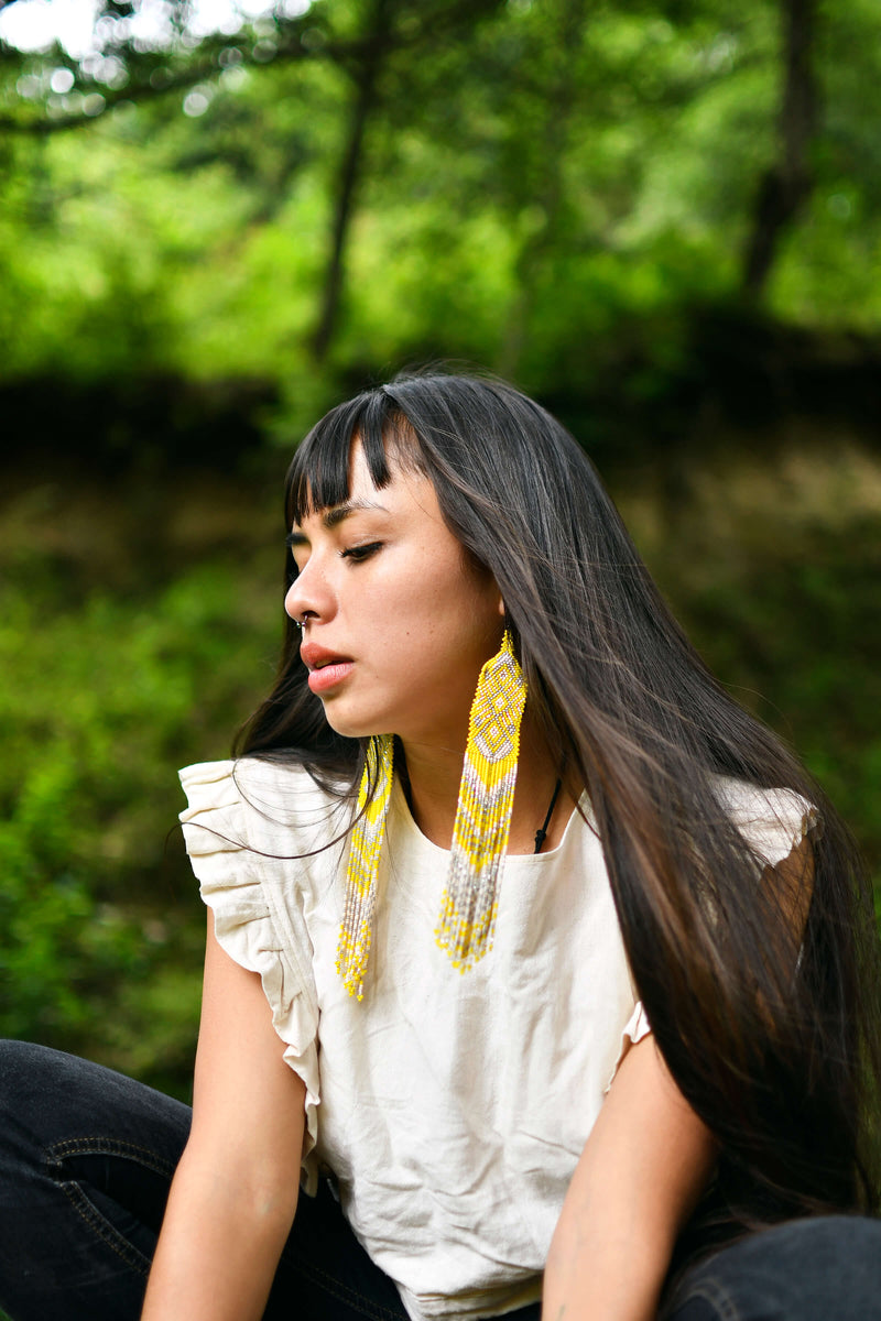 Woman wearing long yellow beaded earrings outside in forest with white shirt