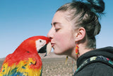 woman wearing red fire bird beaded earrings and kissing a parrot