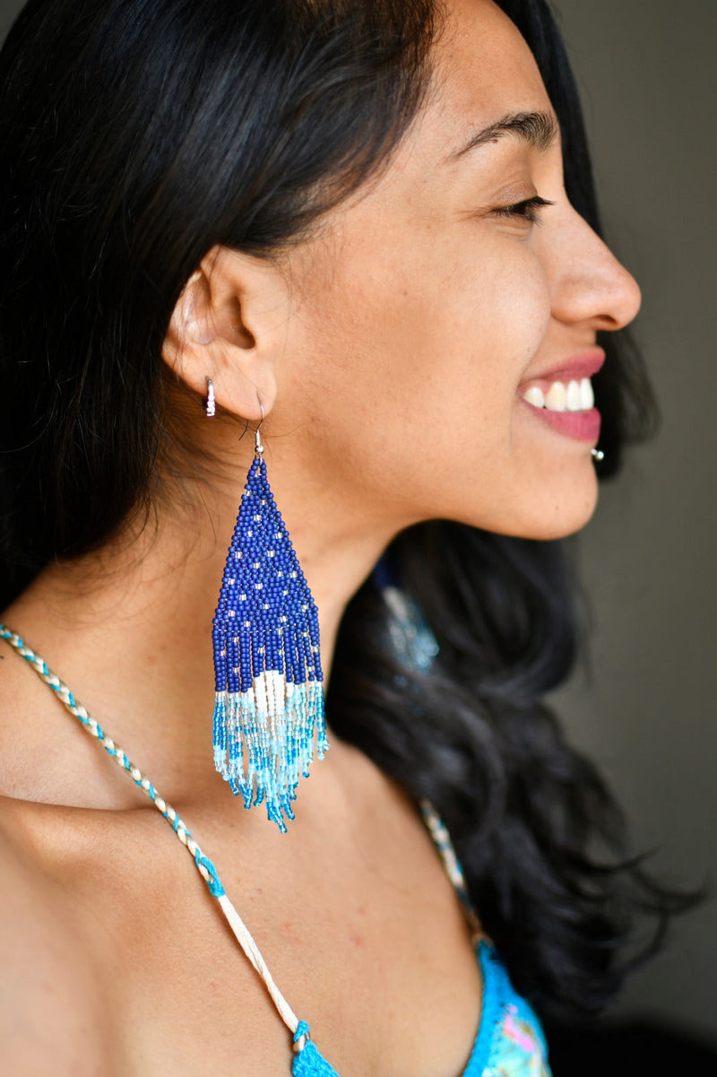 woman smiling wearing blue white stars and moon night sky interstellar fringe beaded earrings