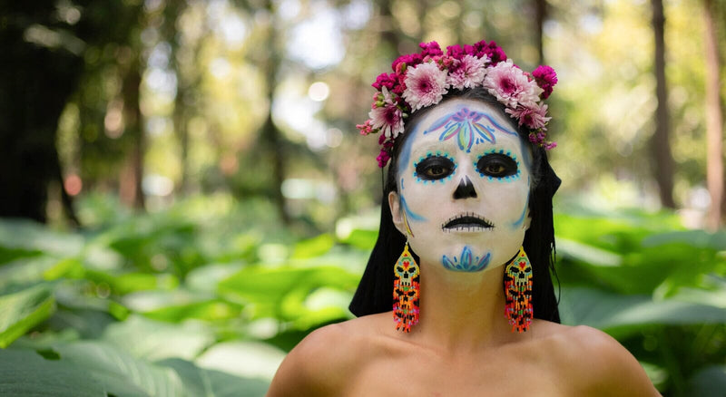 woman in day of the dead makeup wearing skull beaded earrings and a flower crown