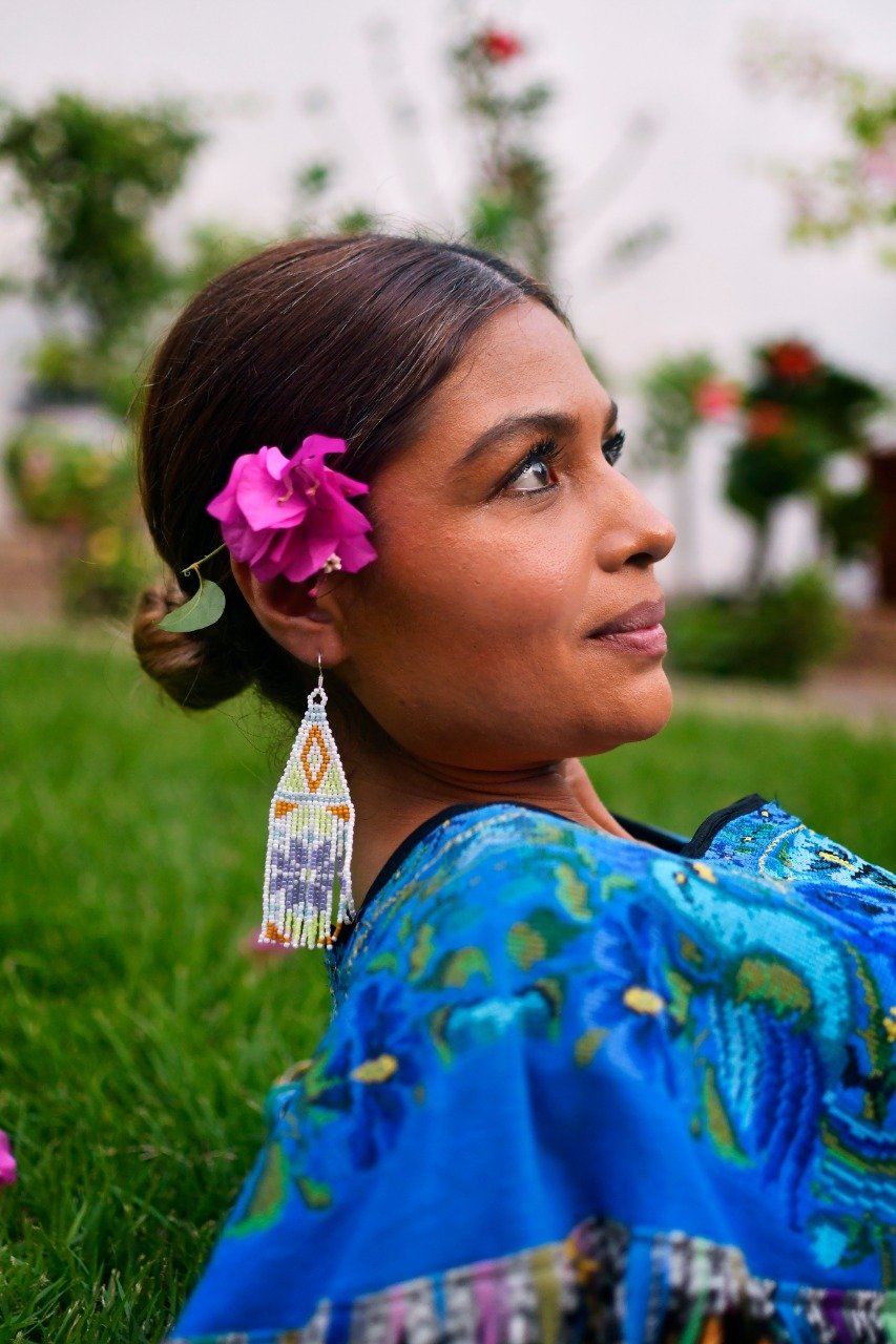 woman wearing white gold light purple fringe beaded earrings on green lawn with pink flower in her hair