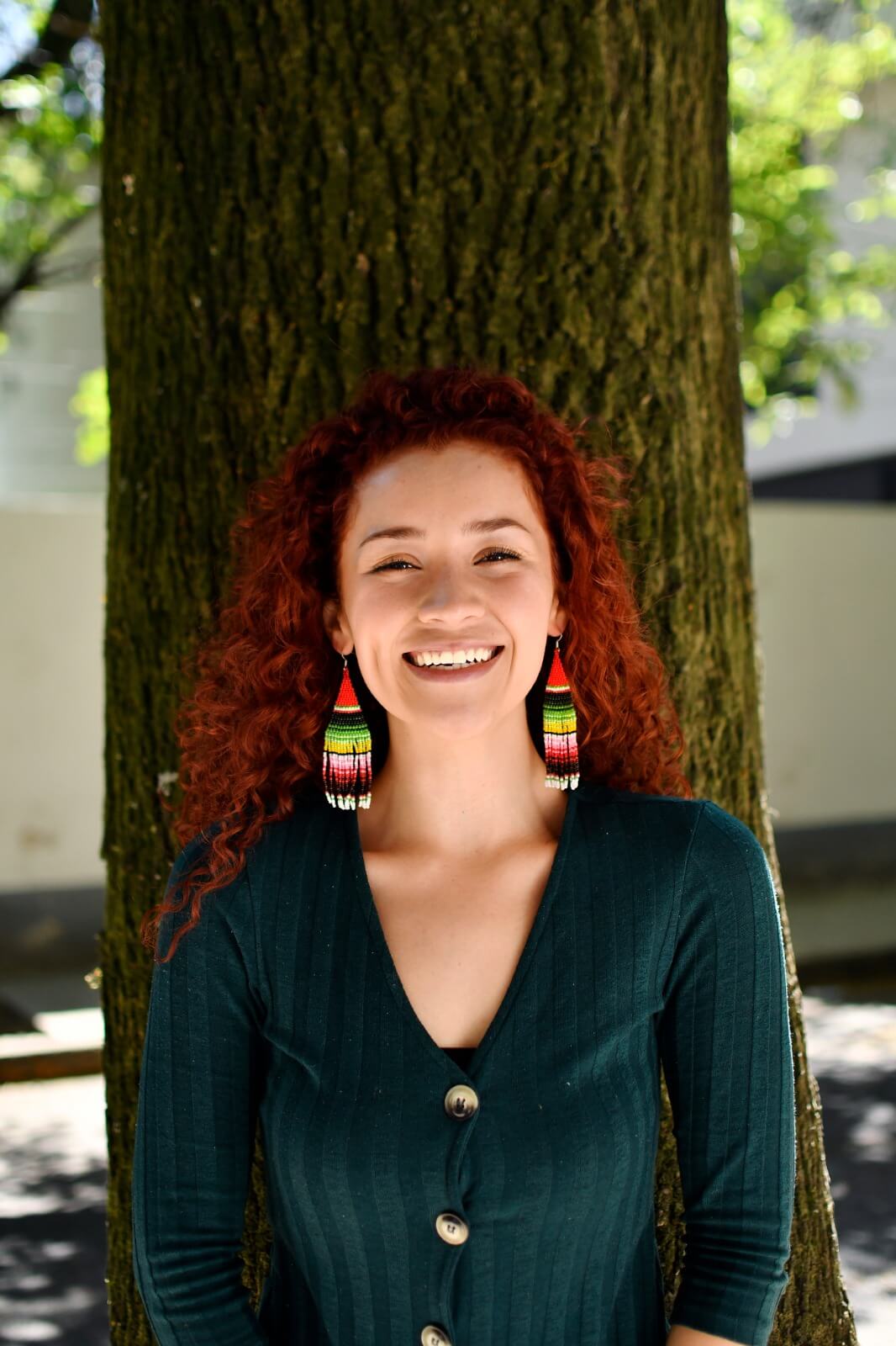woman wearing green red pink yellow white sarape fringe beaded earrings in front of tree